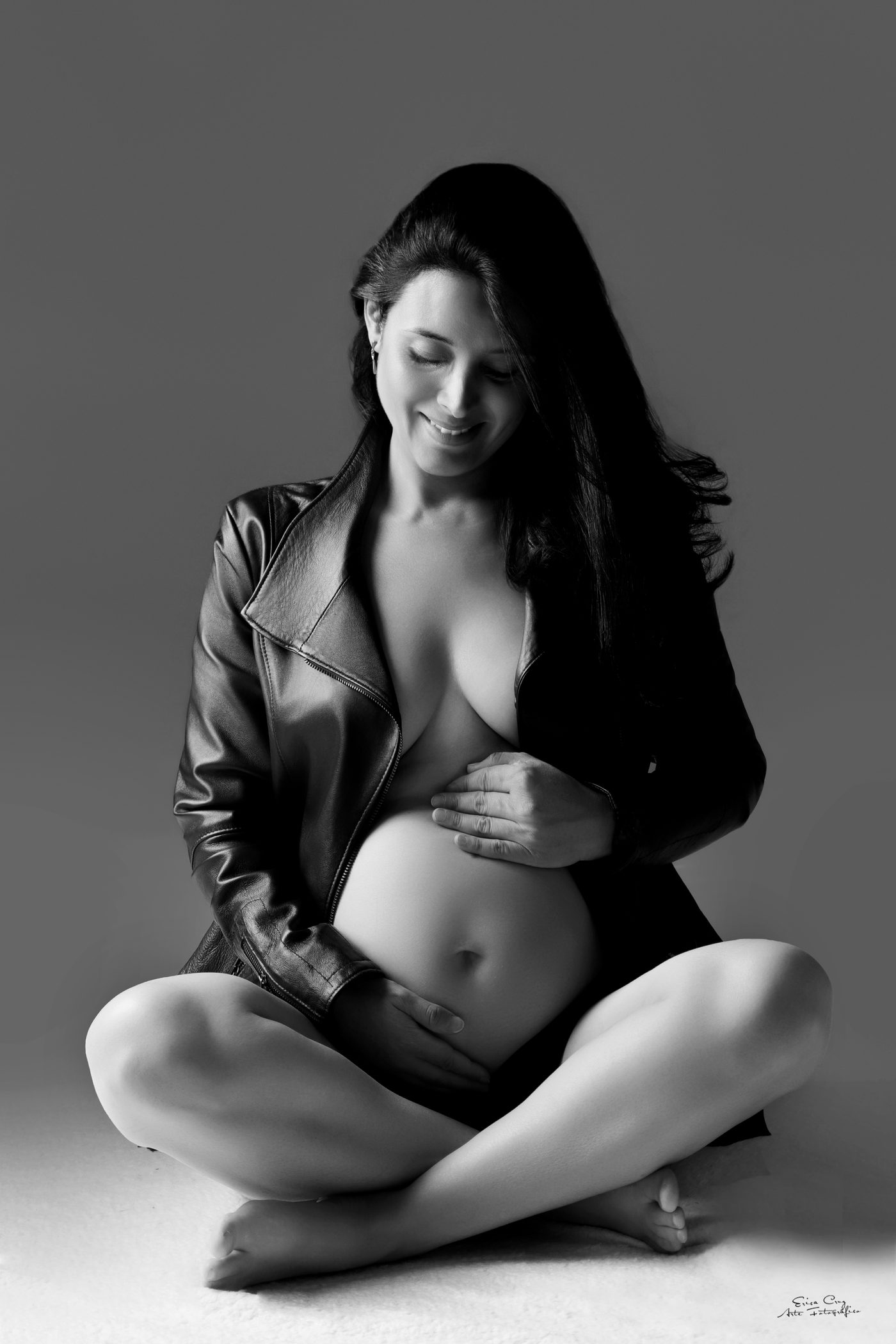 Mujer embarazada con chaqueta de cuero sonriendo a su vientre, blanco y negro, Erica Cruz