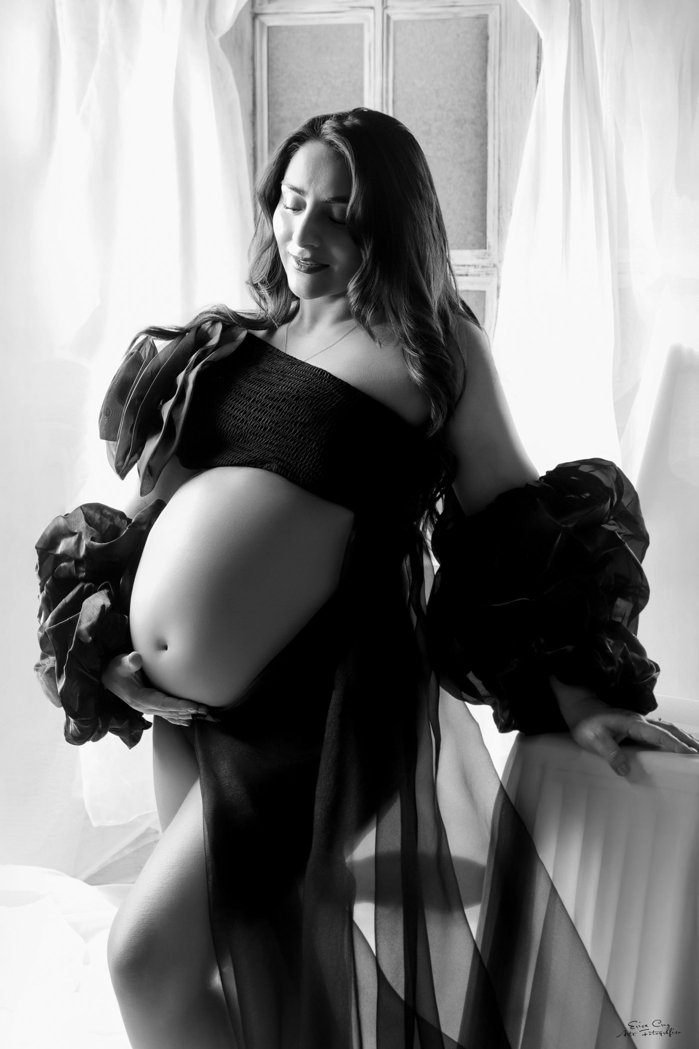 Mujer embarazada junto a una ventana con tul negro, blanco y negro, Erica Cruz