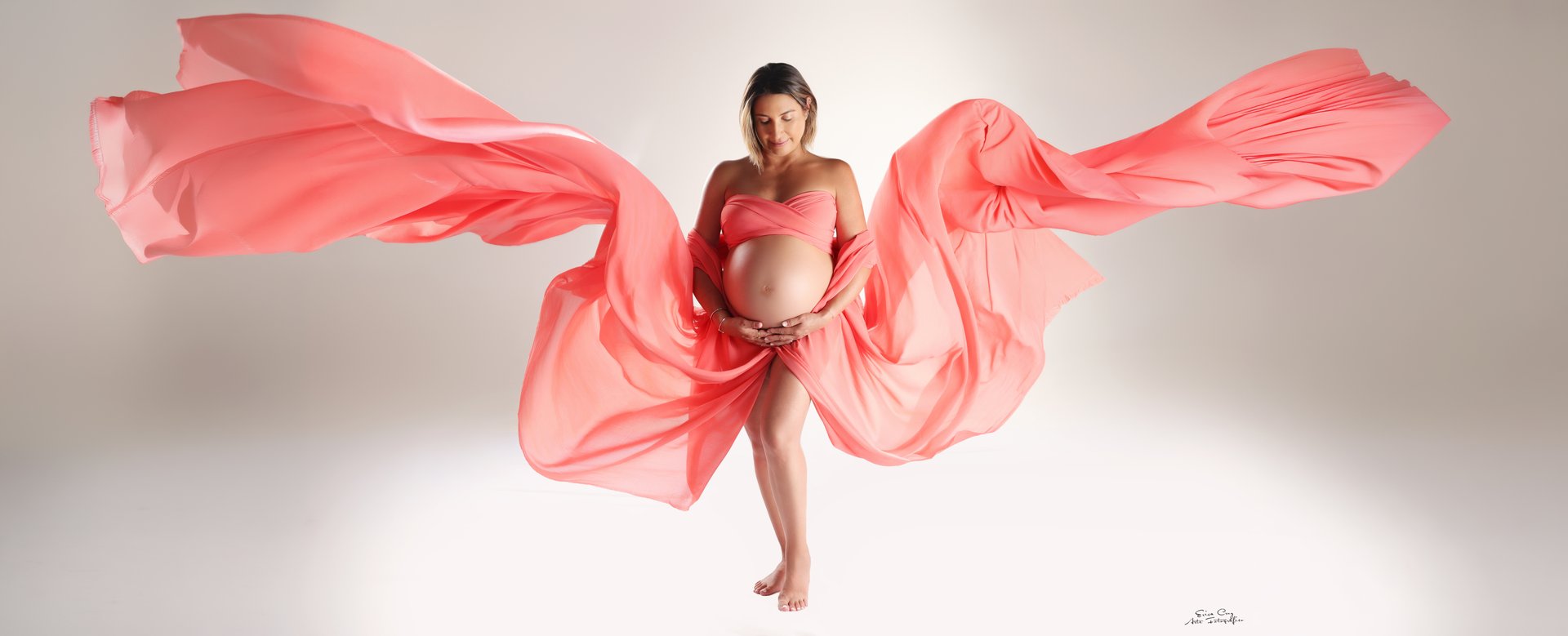 Embarazada con tela coral extendida como alas, Estudio Erica Cruz