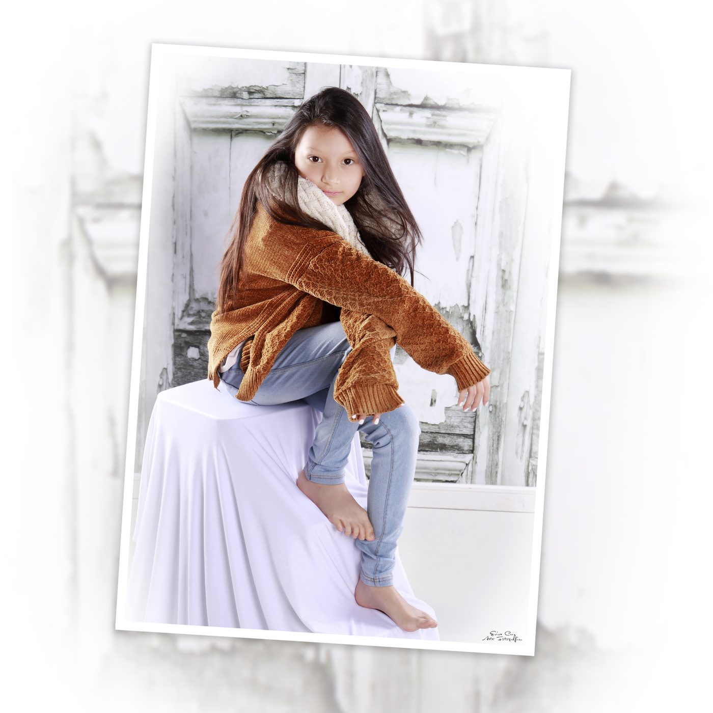 Niña con chaqueta de punto sentada sobre cubo blanco, Erica Cruz