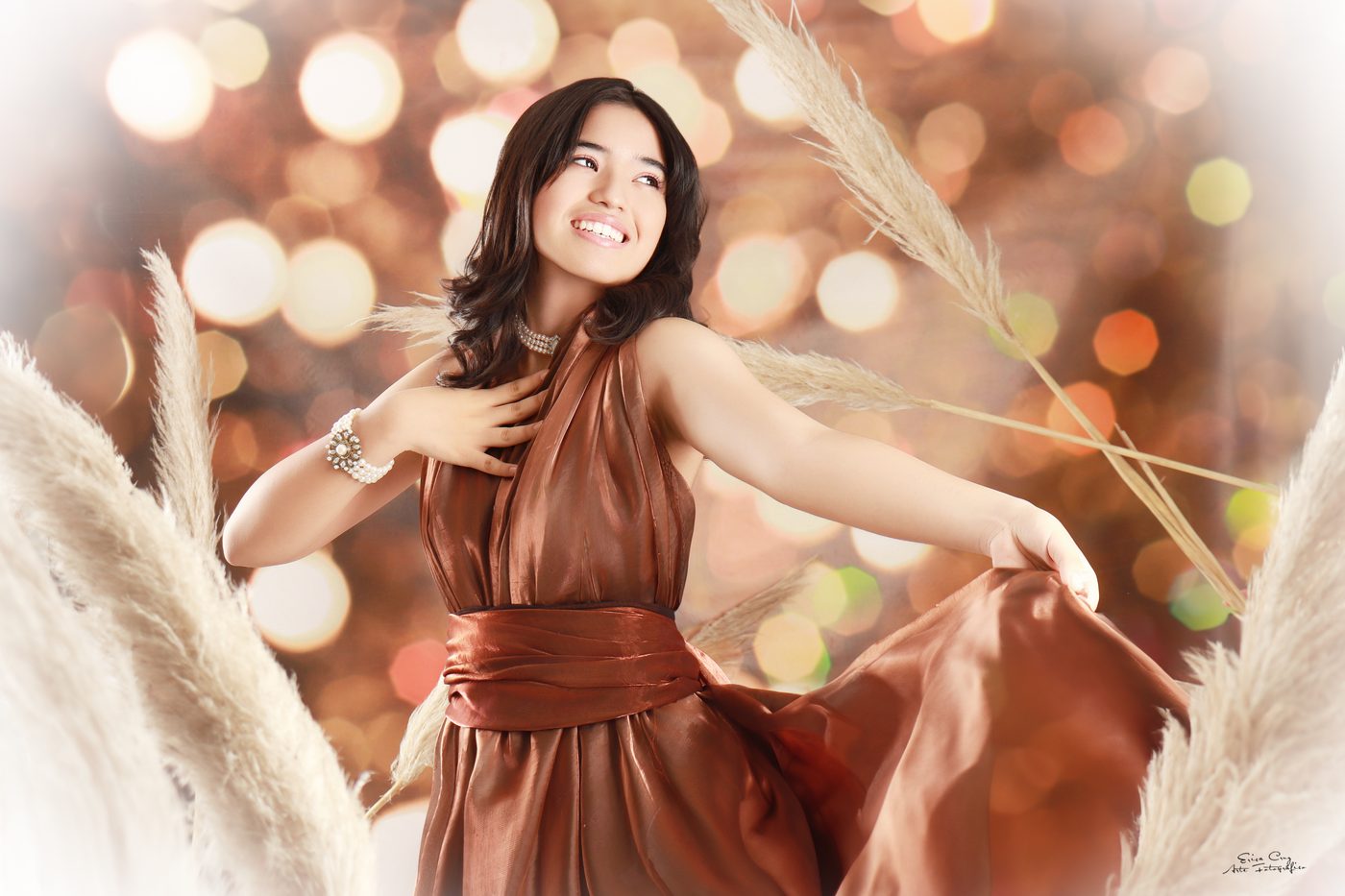 Adolescente con vestido cobre entre plumeros y luces doradas, Erica Cruz