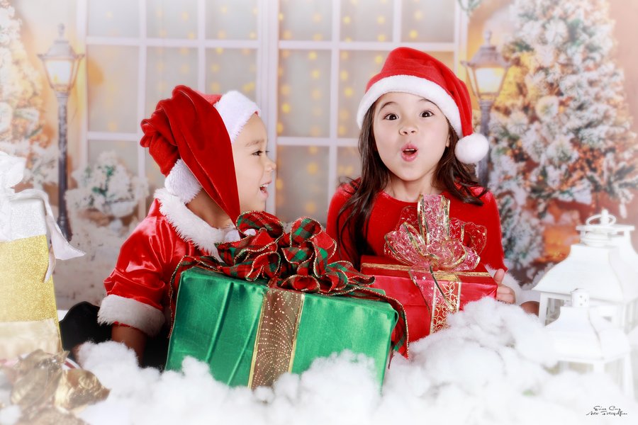 Hermanos con gorros navideños sorprendidos frente a sus regalos, Erica Cruz