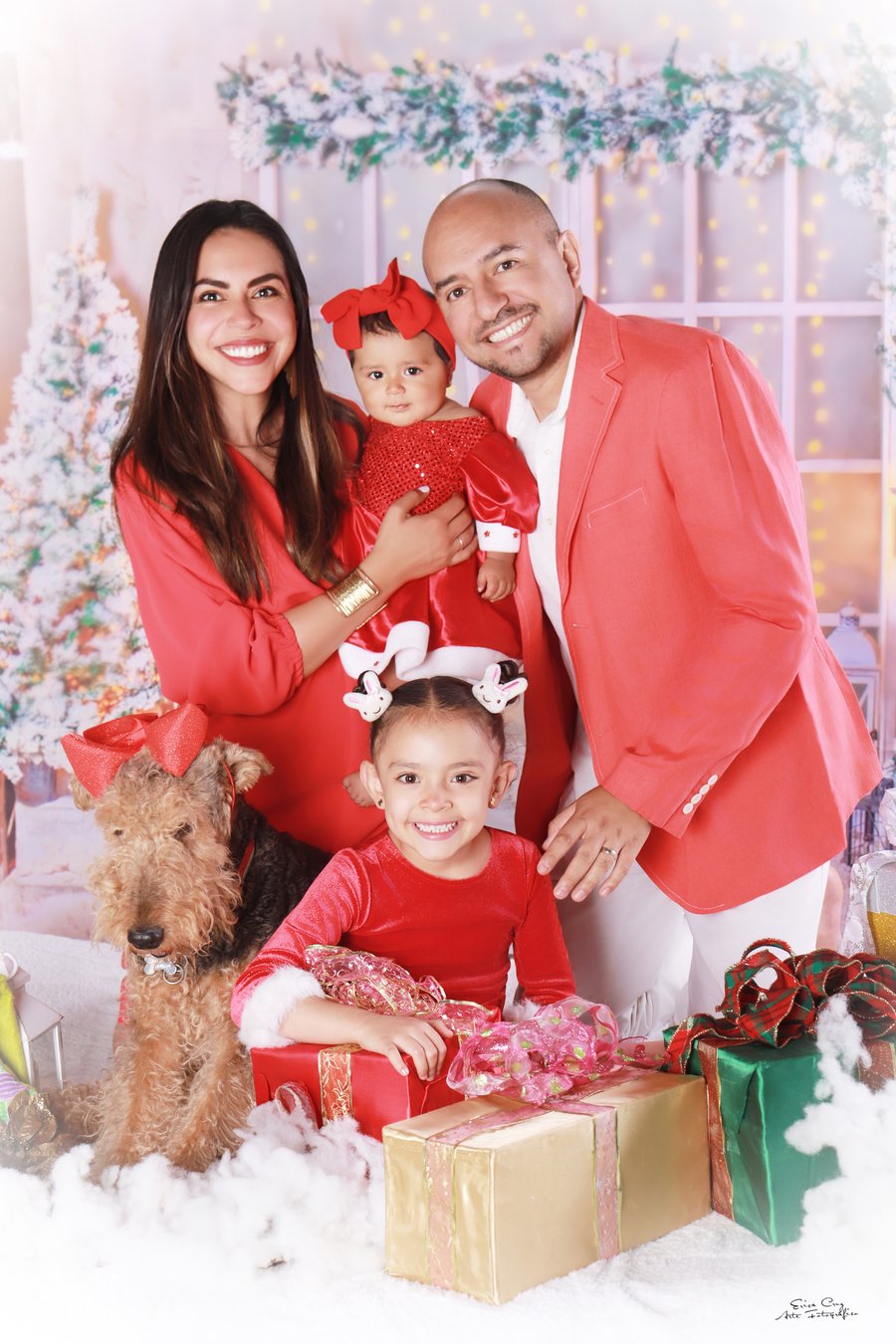 Familia completa vestida de rojo junto a su perro y regalos, set navideño, Erica Cruz