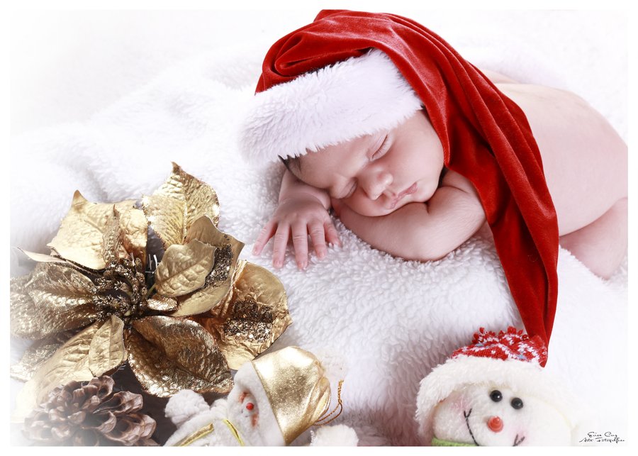 Recién nacida dormida con gorro navideño rojo junto a flor dorada, Erica Cruz