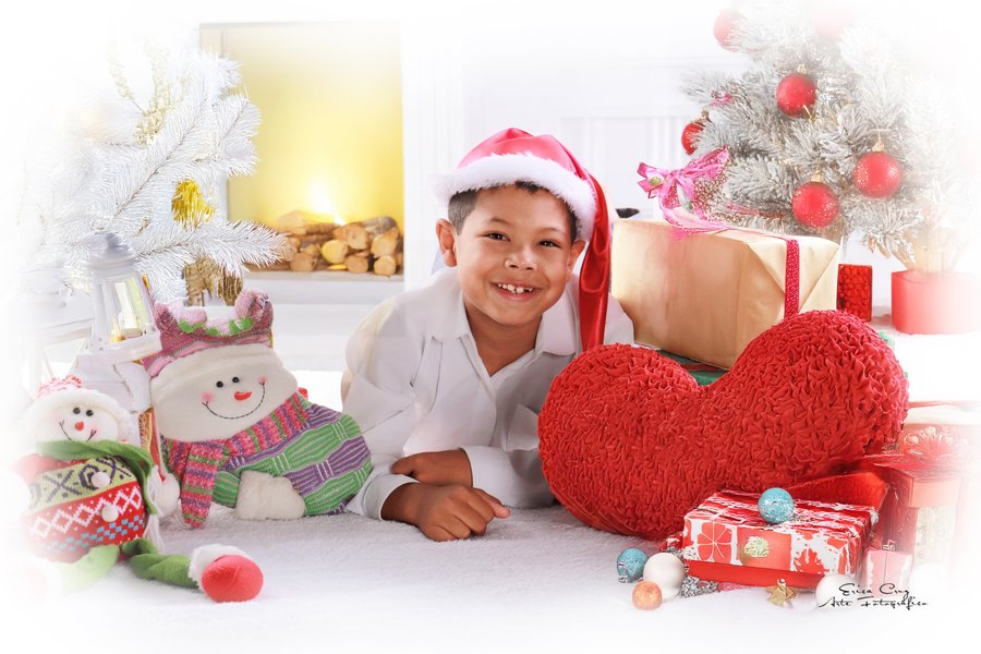Niño con gorro navideño y cojín rojo en forma de corazón, Erica Cruz