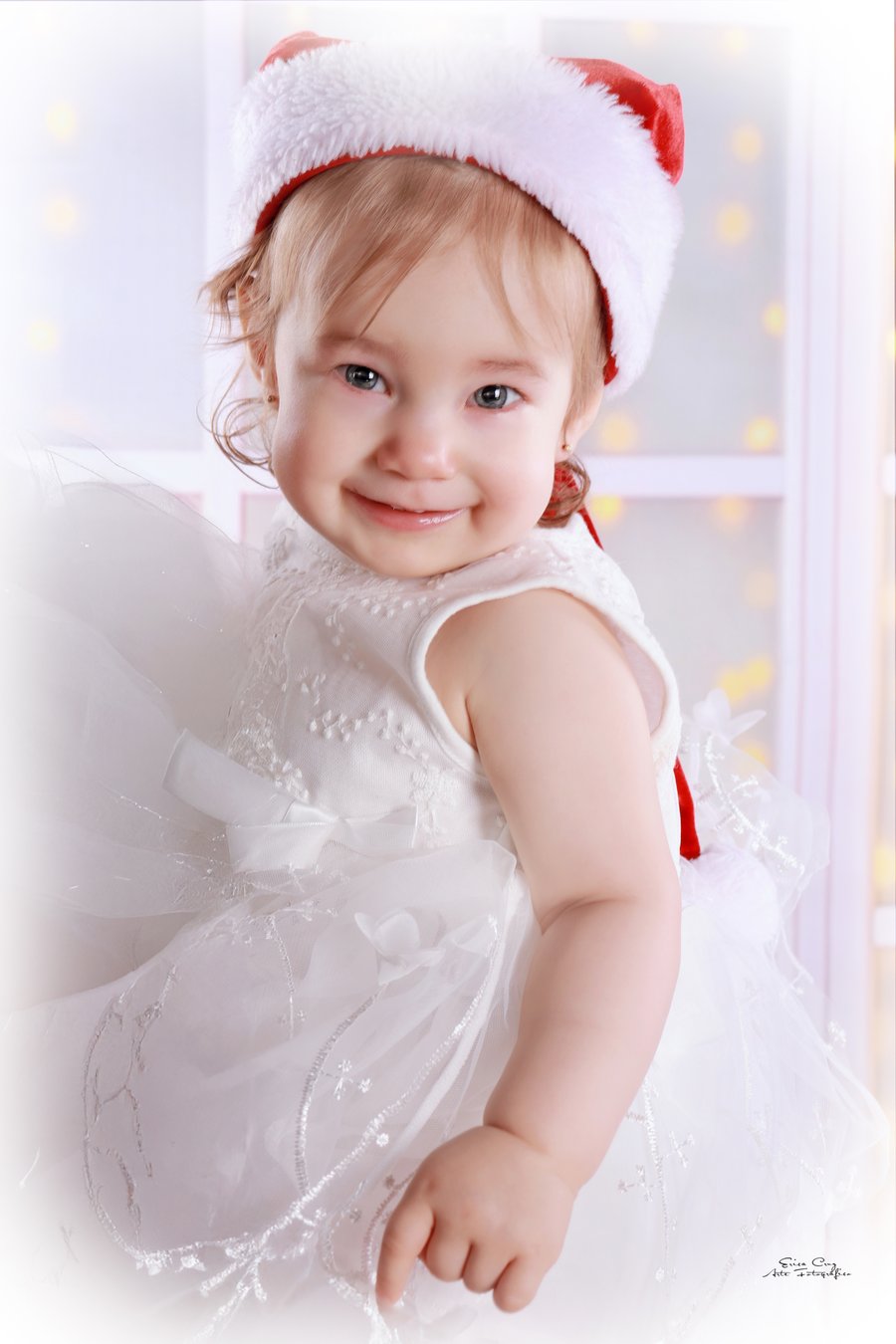 Niña pequeña con gorro navideño y vestido blanco, Erica Cruz